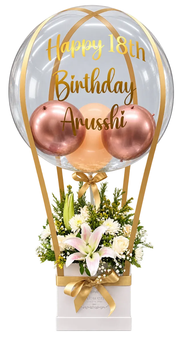 Hot air balloon bubble balloon with rose gold balloons, gold Happy 18th Birthday lettering and a box of white lilies and roses